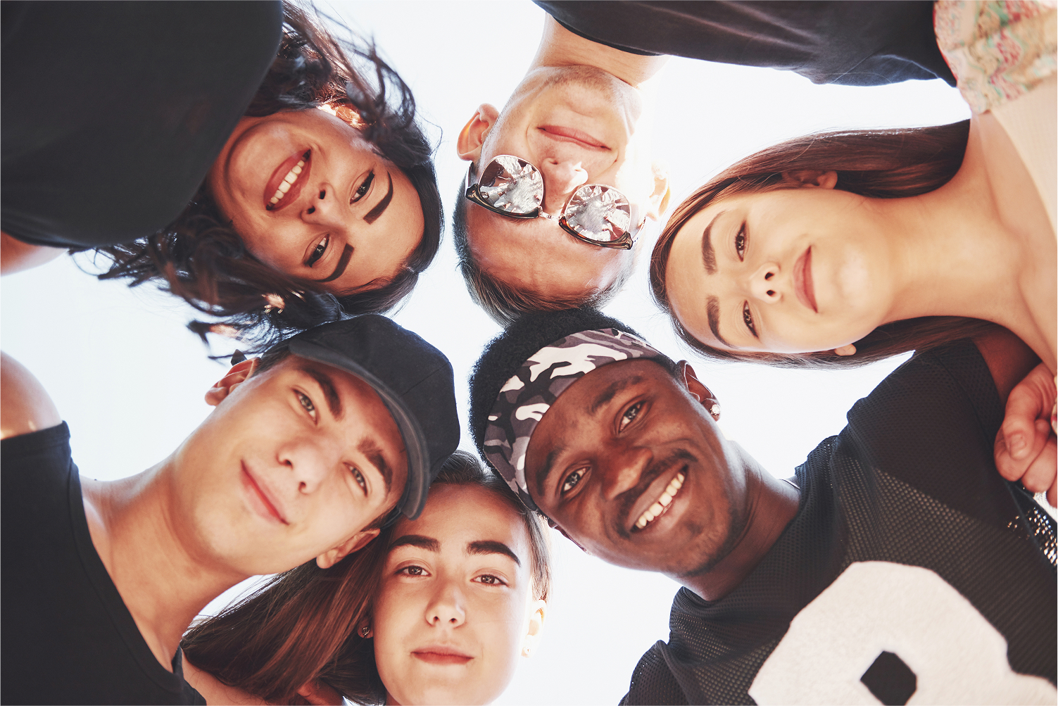 Group of diverse students huddled in a circle looking down at the camera and smiling