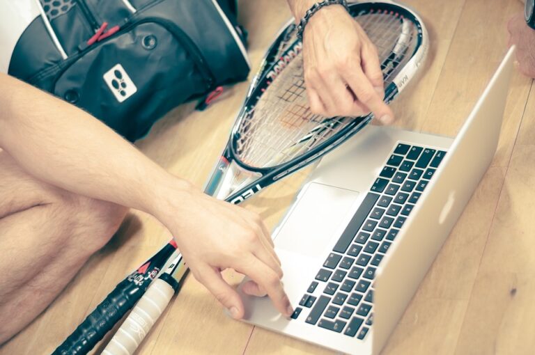 Two squash players with their equipment gathered around a laptop computer