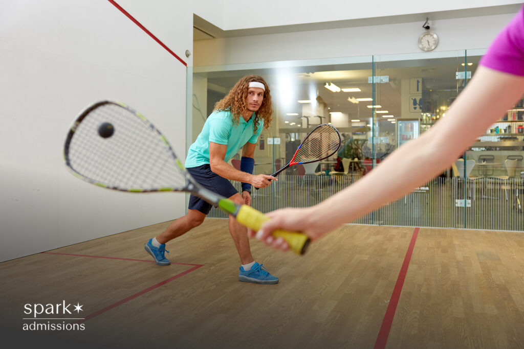 A male athlete playing squash, preparing to return a serve in an indoor court