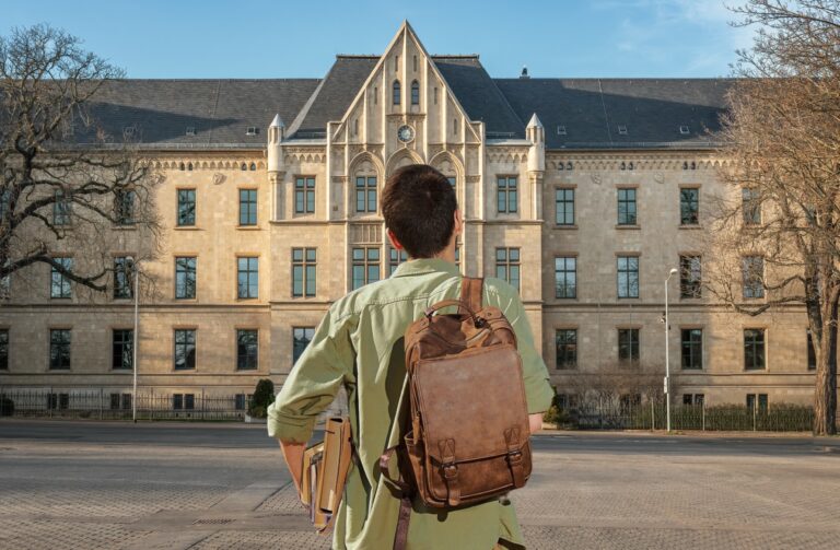 A student with a brown backpack standing in front of a large historic college building