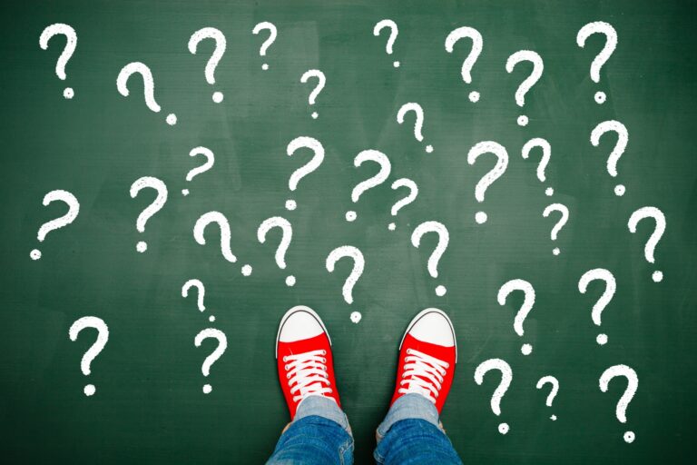 Someone standing on a chalkboard covered in question marks.