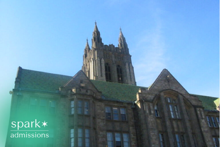 Historic Gothic-style university building with a tall stone clock tower and academic campus architecture under a clear blue sky.