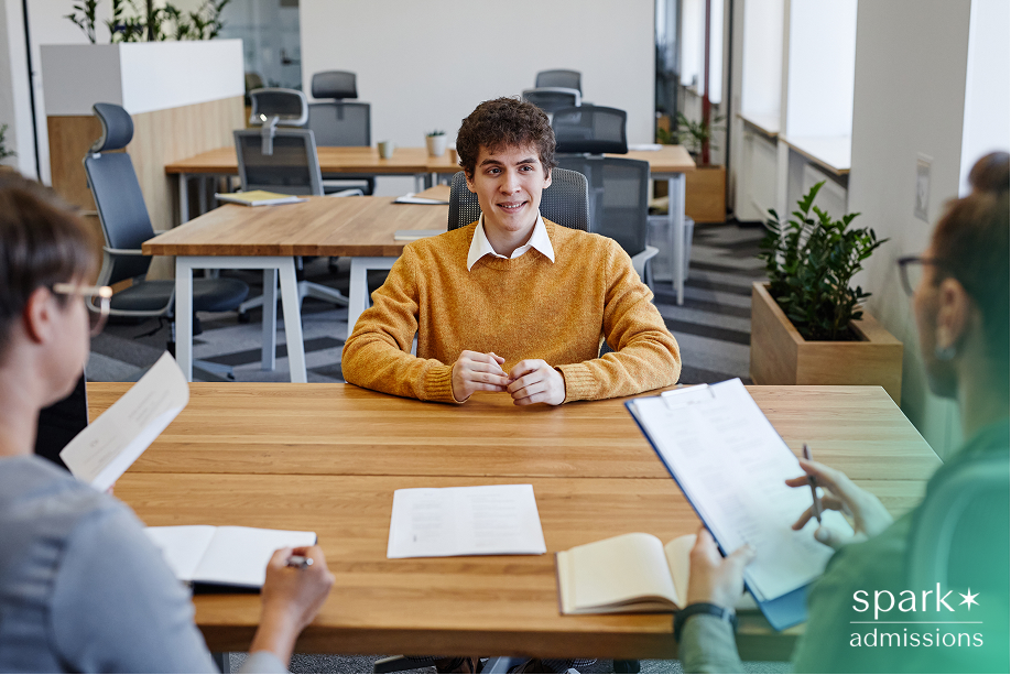 Young man in a yellow sweater being interviewed by three people at a table in an office setting