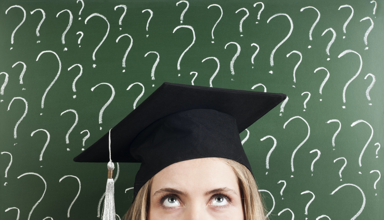 A graduating senior in her cap standing in front of a chalk board covered in question marks