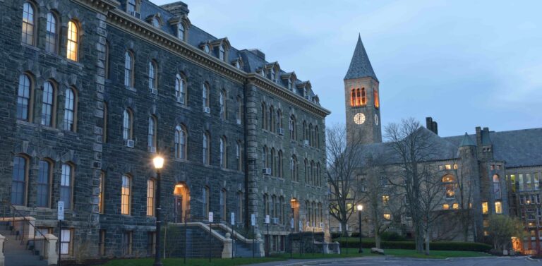 The exterior of several stone-faced buildings at dusk, just as the lights are coming on.