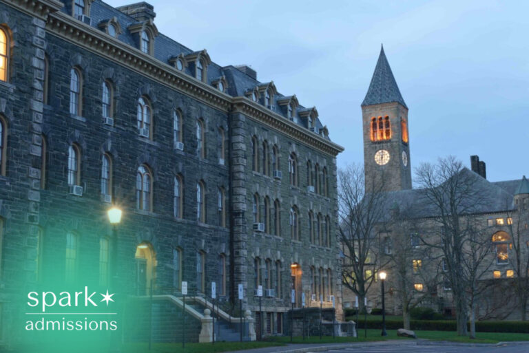 Historic university campus with a stone academic building and illuminated clock tower at dusk under a blue evening sky.