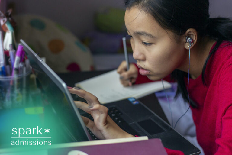 Student using a laptop with earphones while taking notes at a study desk during an online class or remote learning session.