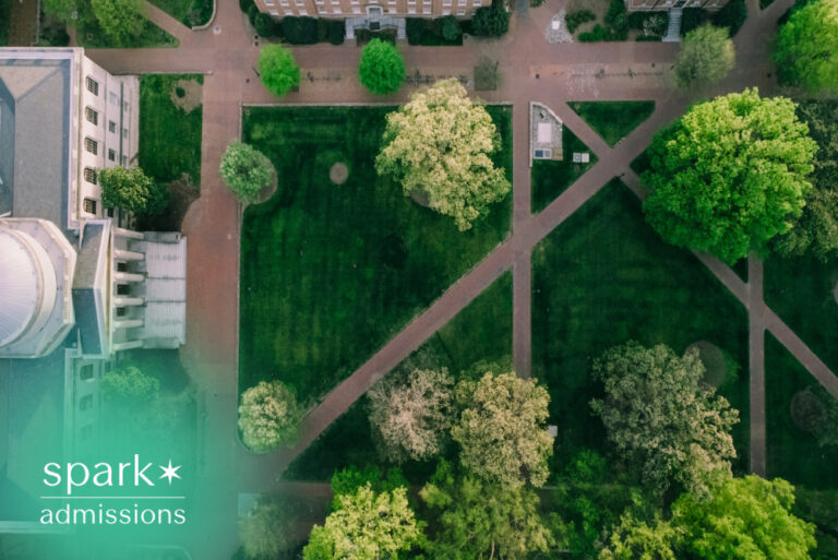 Aerial view of a college campus quad with tree-lined walkways, academic buildings, and landscaped green spaces surrounding the central lawn.