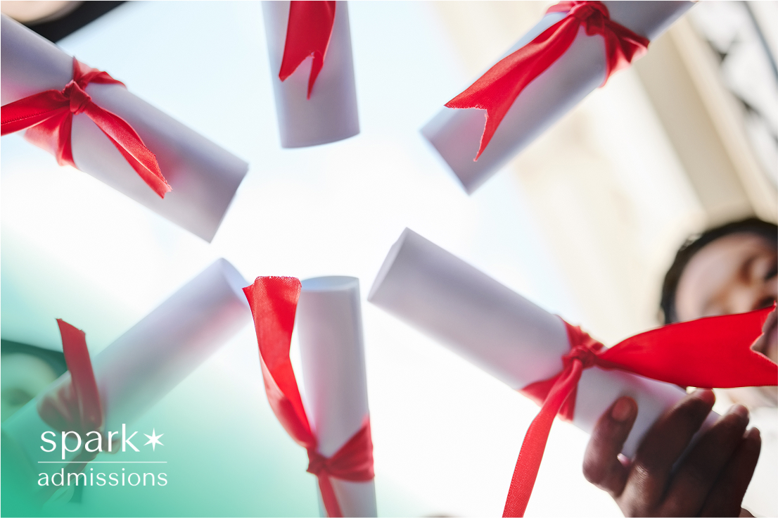 Students holding rolled diplomas with red ribbons in a circle against the sky