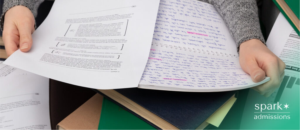 Student hands holding typed pages and handwritten notes surrounded by open books