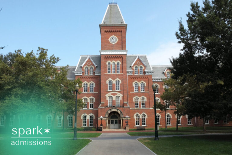 Historic university campus building with a central clock tower and landscaped grounds on a sunny day.