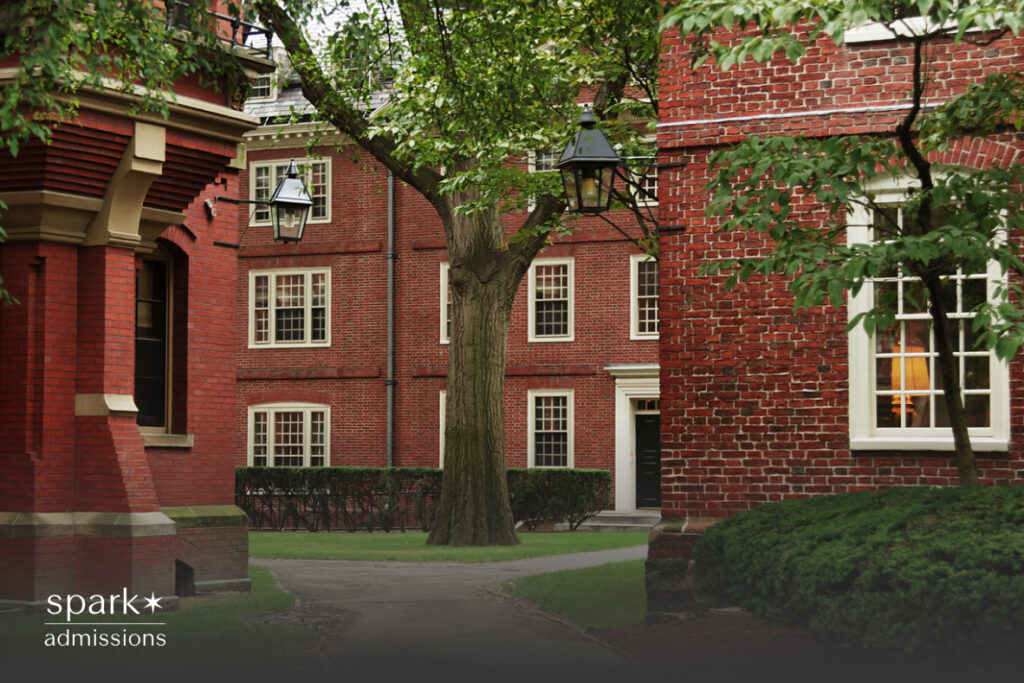 A quiet courtyard sits between classic red brick college dorms with black doors and hanging lanterns