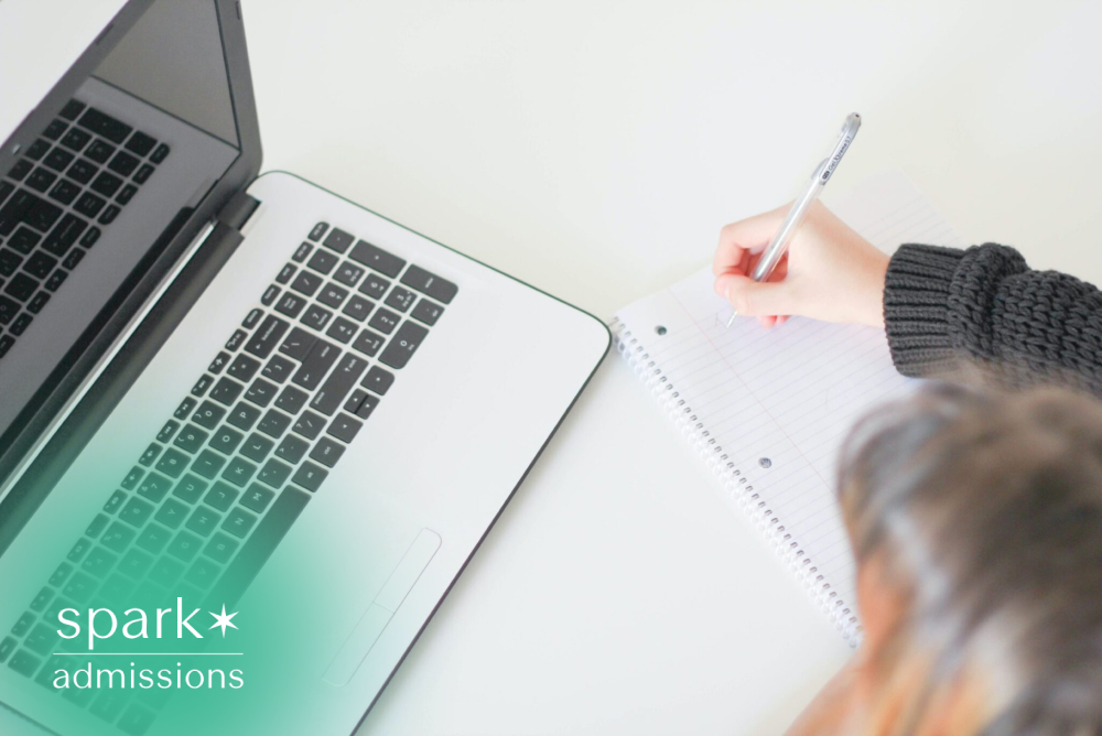 Student taking handwritten notes beside a laptop during an online study session.