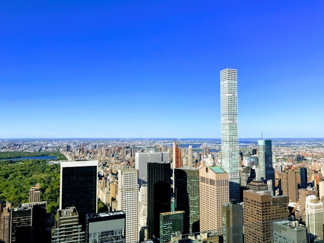 An aerial view of Manhattan with New York University and towering skyscrapers on the right under a vibrant blue sky, highlighting an urban setting for higher education