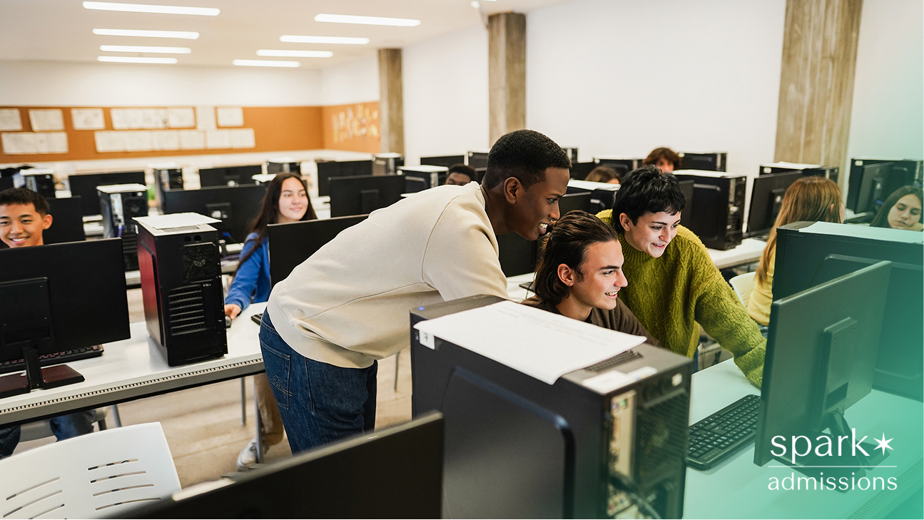 A students in a computer lab smiling and working together at desktop monitors