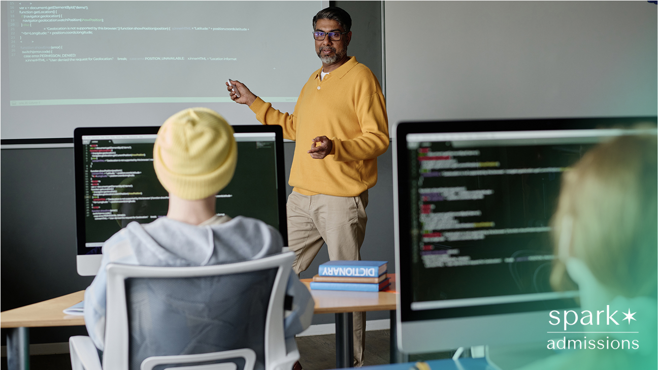 Instructor in yellow sweater teaching a programming class with code projected on a screen