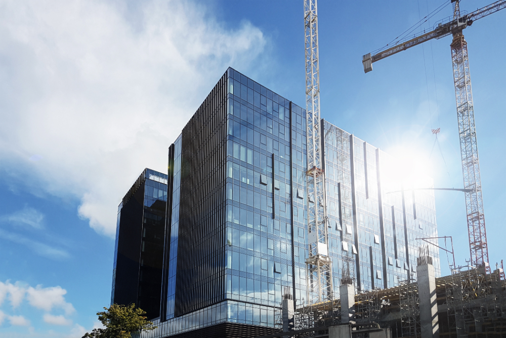 Modern glass office building under construction with cranes and clear blue sky