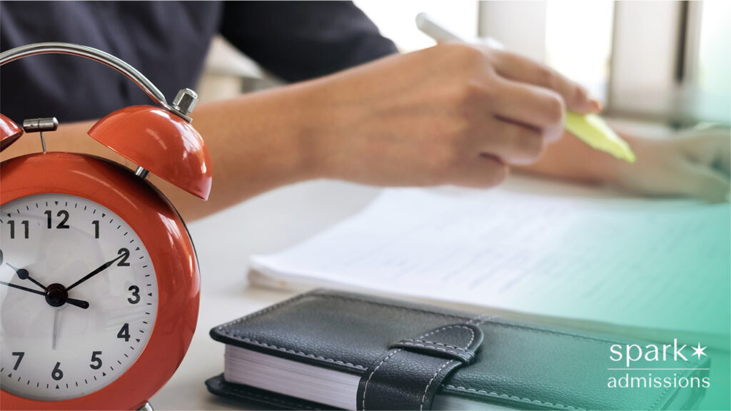 Close-up of an orange alarm clock, planner, and a hand highlighting notes on paper
