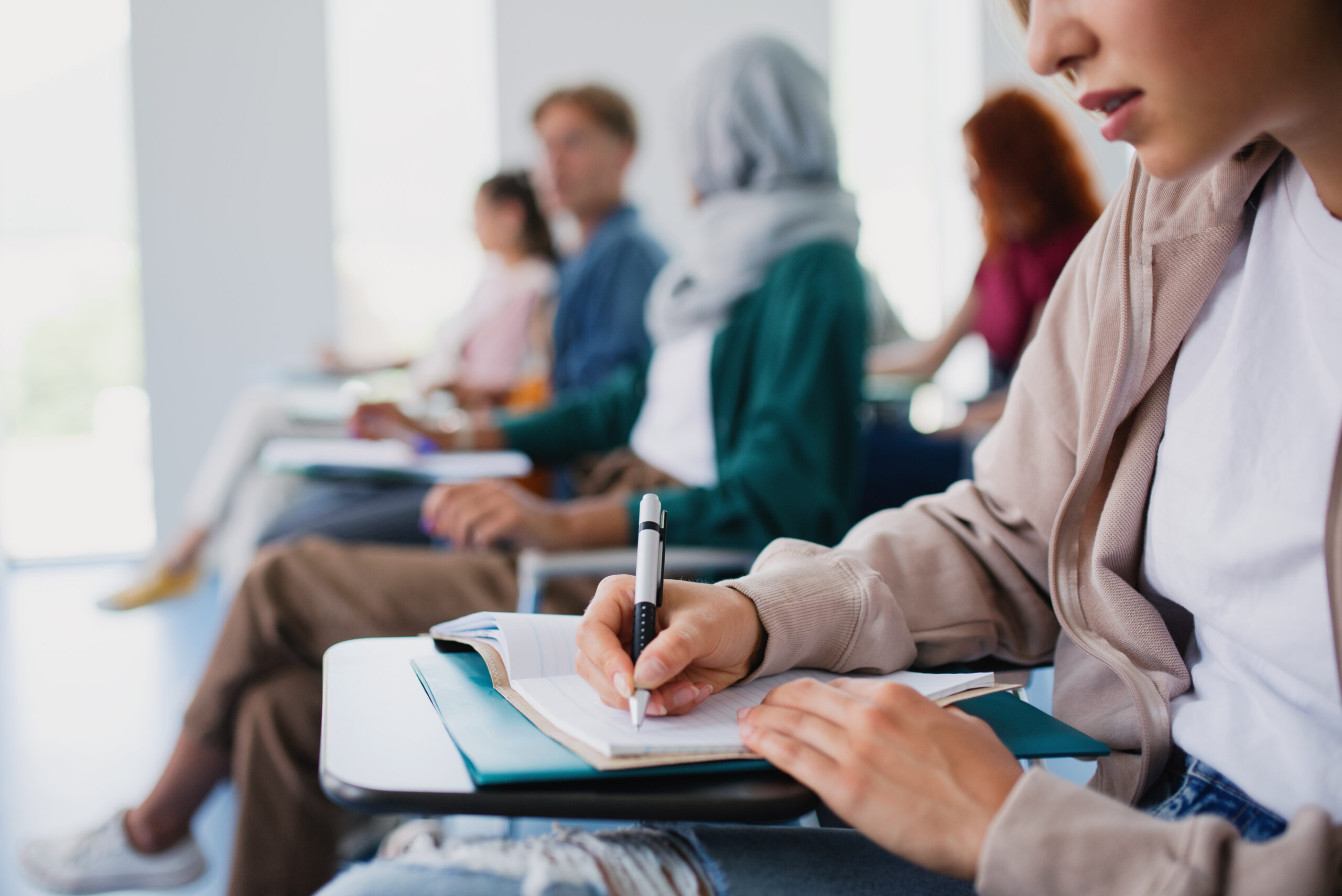 Close-up of students in a classroom writing in notebooks on individual desks