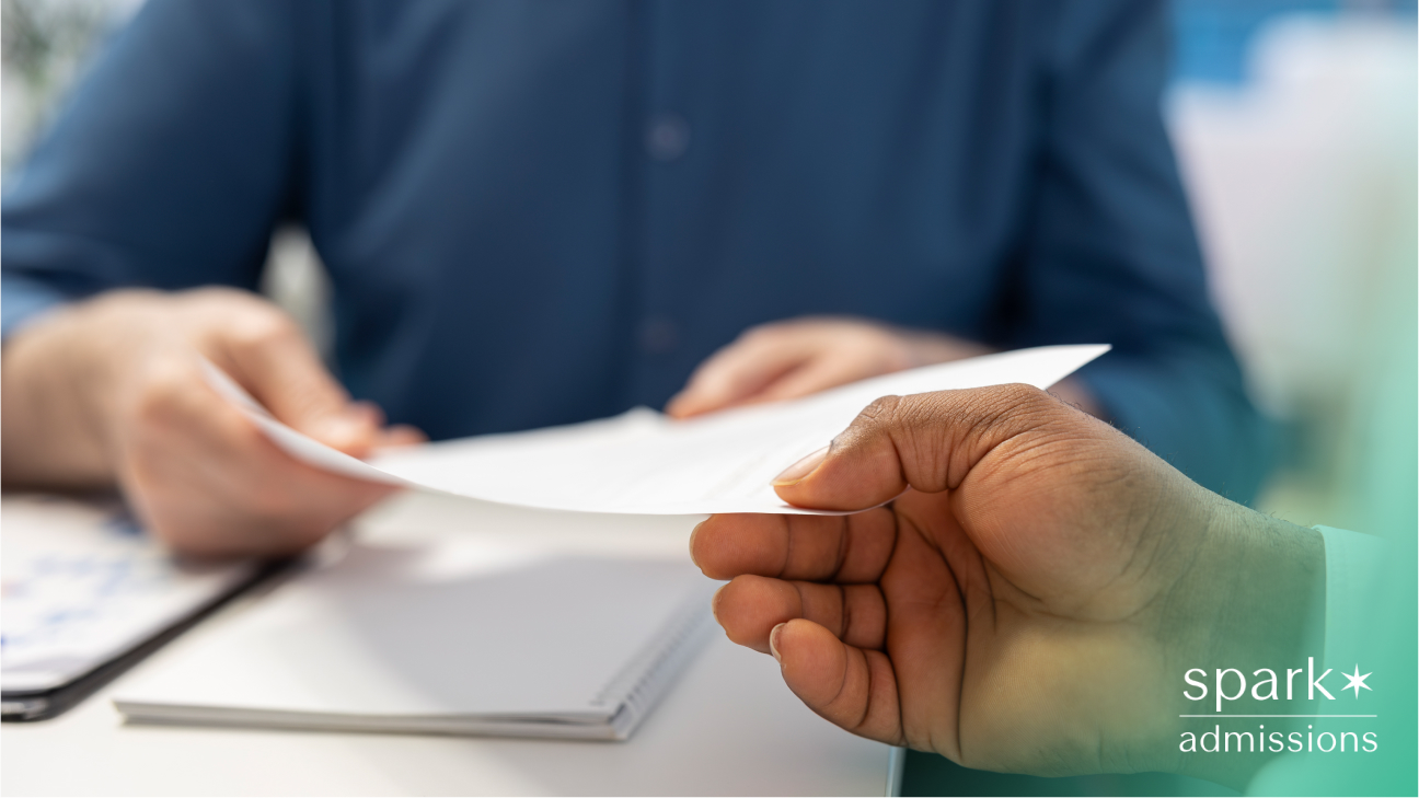 A person handing over a paper to someone in an office setting with a notebook and folder on the table