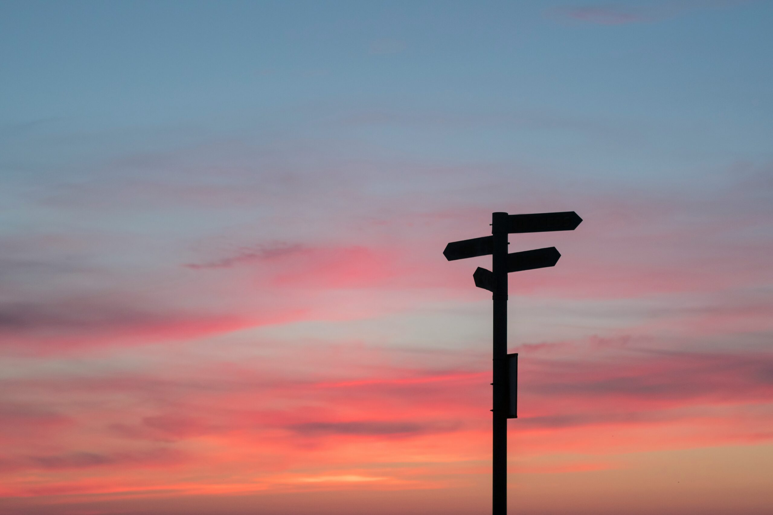 A directional signpost silhouetted against a vibrant pink and blue sunset sky