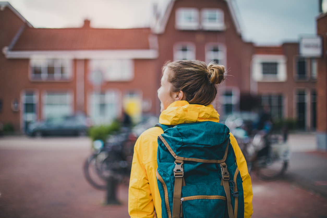 A student wearing a yellow jacket and teal backpack looks toward a campus building with bikes nearby
