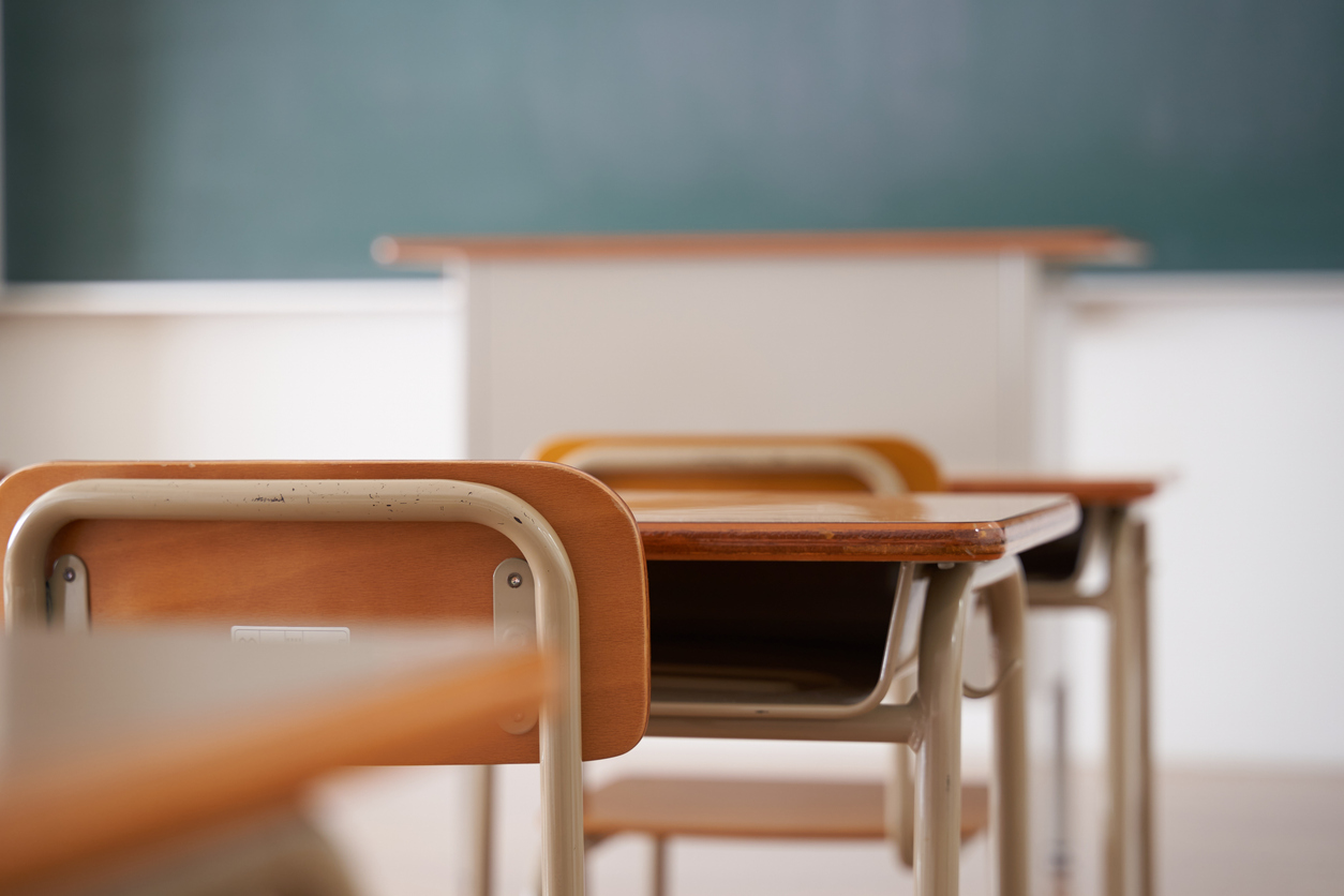 Empty classroom desks and chairs with a chalkboard and teacher's podium in the background