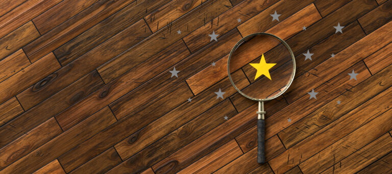 A magnifying glass highlighting a gold star among gray stars on a wooden surface, symbolizing selection or recognition