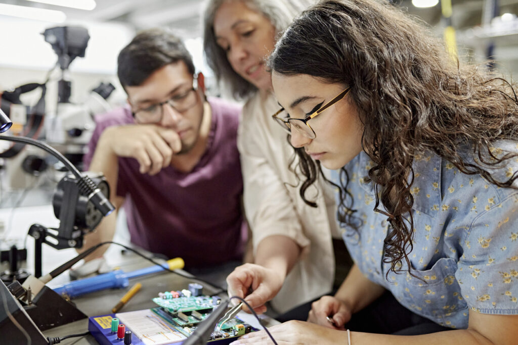Two students and a professor collaborate on a circuit project in a science lab with technical equipment