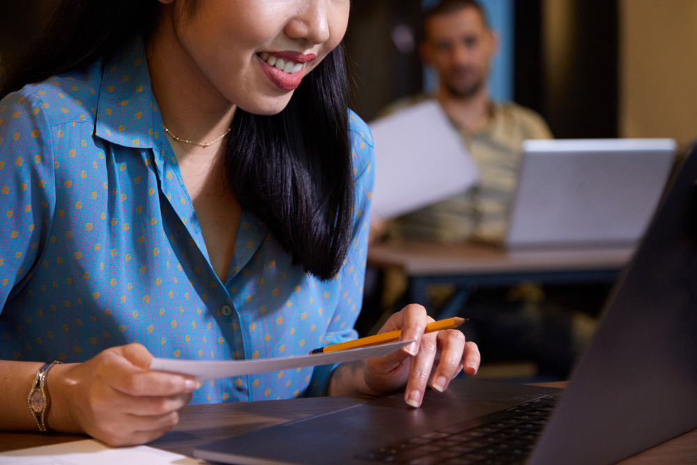 A student smiles while reading documents in front of her laptop during a classroom session with others in the background