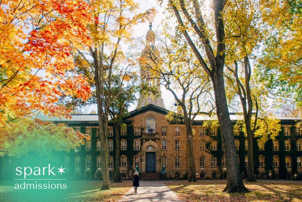 Historic Ivy League university campus building surrounded by colorful autumn trees, with a student walking along a tree-lined path on a sunny fall day.