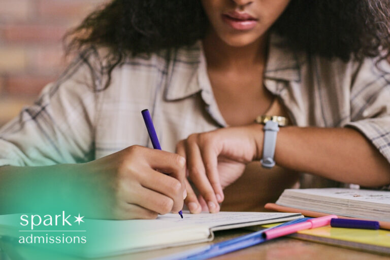 College student writing study notes in a notebook at a desk with textbooks, colorful highlighters, and school supplies while preparing for classes or exams.