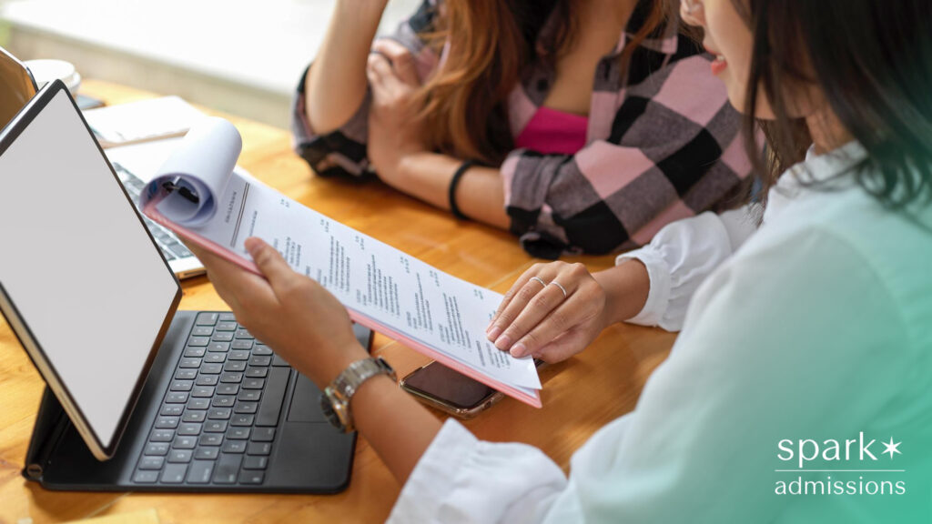 A student and advisor go over a printed resume next to a tablet and laptop during a consultation at a table