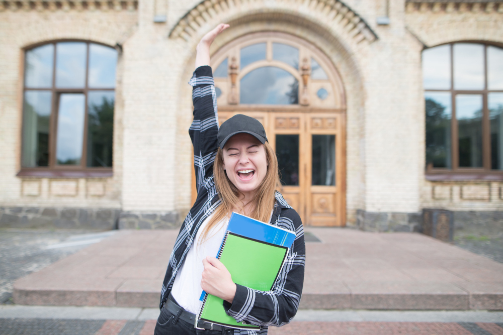 A student raises her arm in celebration while standing outside a university building