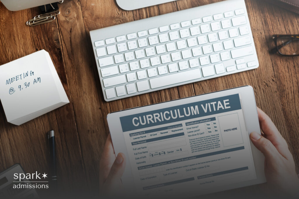 A tablet displays a curriculum vitae next to a keyboard, notepad, and sticky note with a meeting reminder