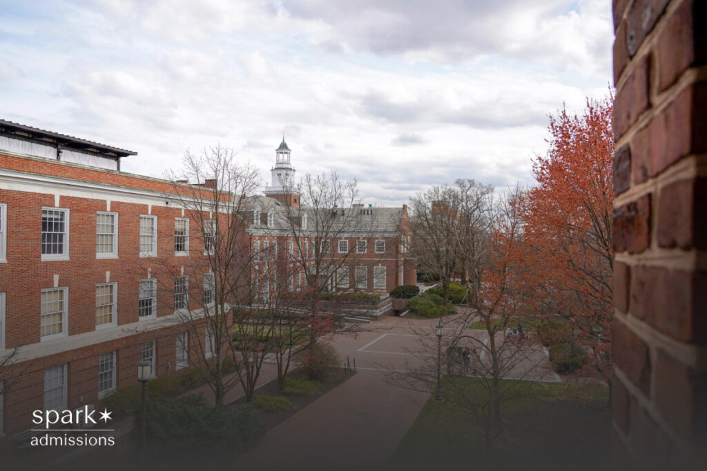 A quiet college courtyard features red-brick buildings, bare trees, and a cloudy sky