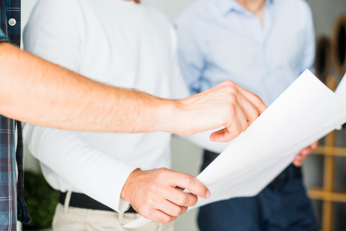 Three individuals stand side by side pointing at a large sheet of white paper, reviewing a document