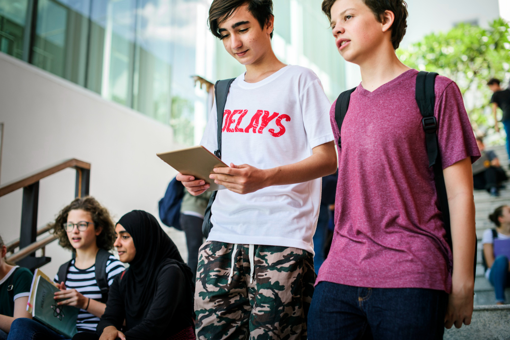 Two male students walk down stairs chatting, while others sit reading and studying in the background