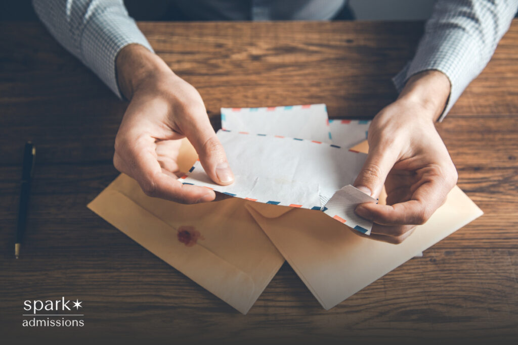 A person opens a paper envelope on a wooden desk with another sealed envelope beside it