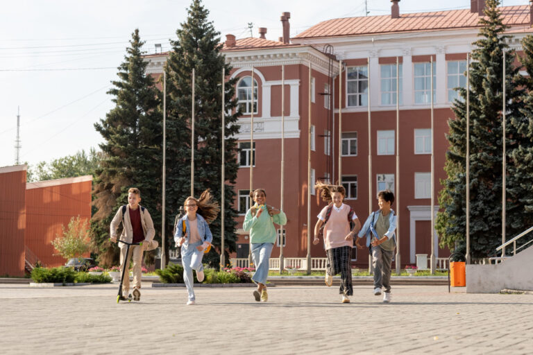 Five children run excitedly toward the camera in front of a red brick school building