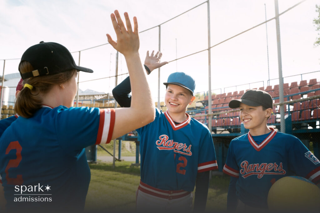 Three kids in baseball uniforms smile and celebrate with a high five on the field