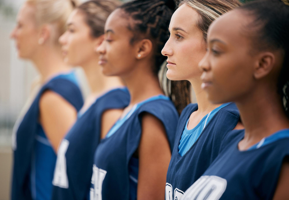 A row of focused female basketball players stands in matching blue uniforms, facing forward