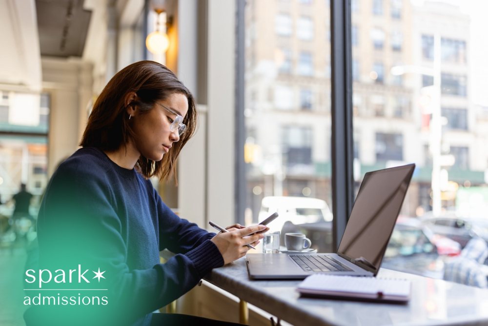 Student using a laptop and smartphone while studying in a café, researching colleges and working on college applications in a modern urban setting.