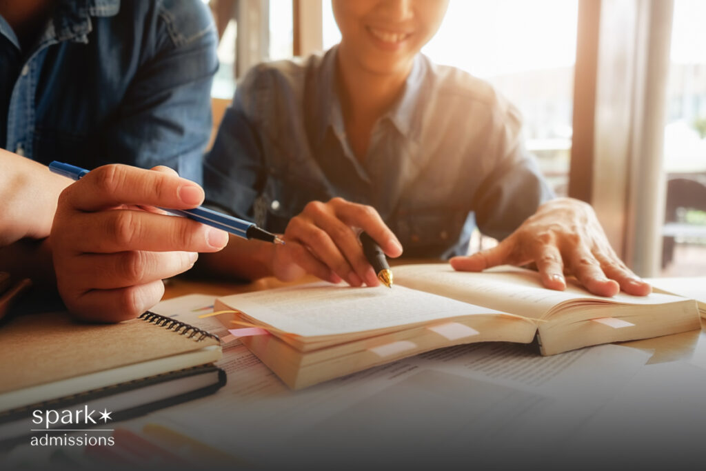 Two people read and take notes together at a table with open textbooks and highlighters