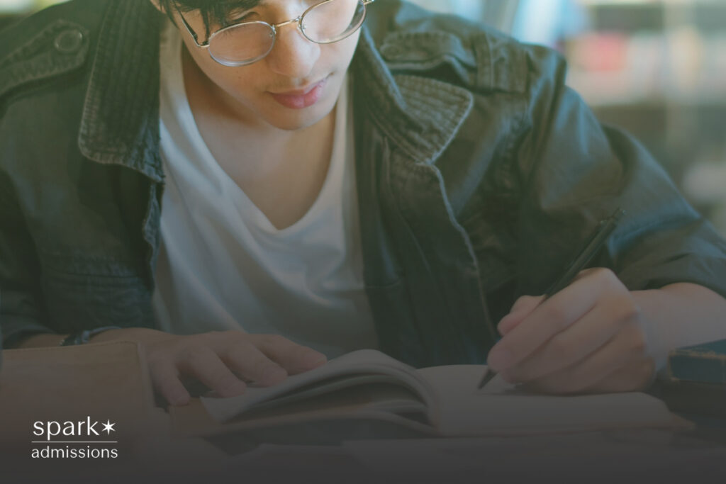 A male student focuses on writing in a notebook while studying at a table