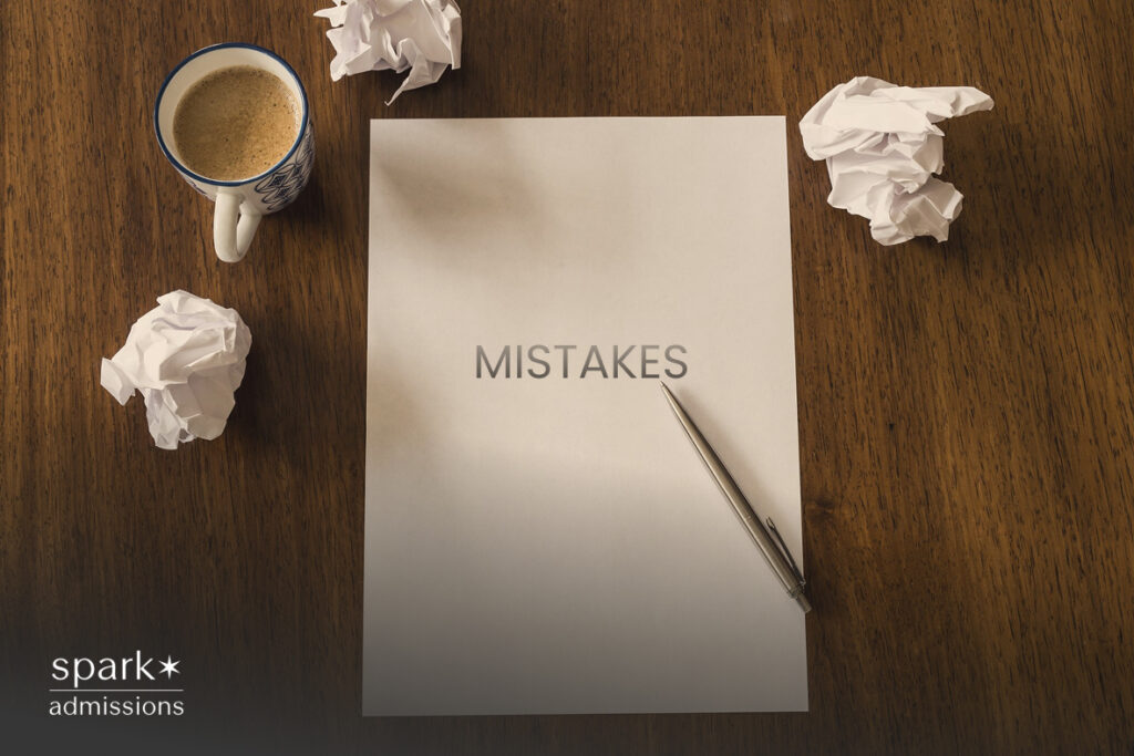 Paper titled 'Mistakes' on a wooden desk, surrounded by crumpled drafts and a coffee cup