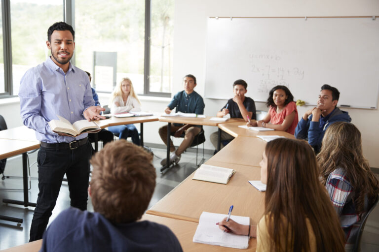 A male student standing at the front of a classroom, leading a discussion with engaged students