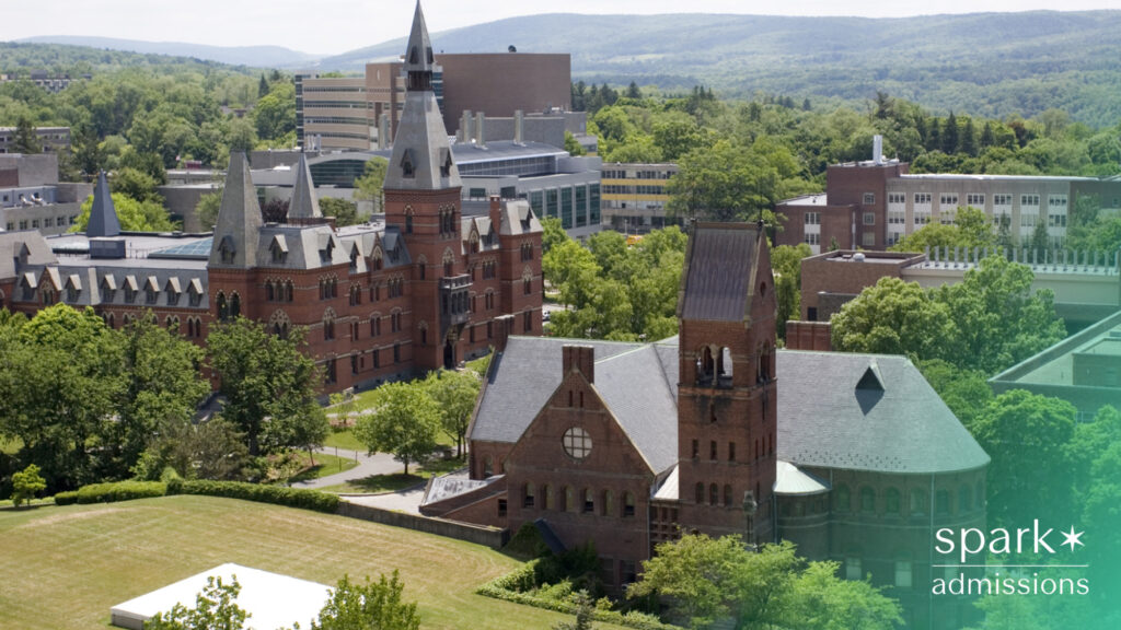 An aerial shot shows a college campus with red-brick buildings surrounded by trees and hills