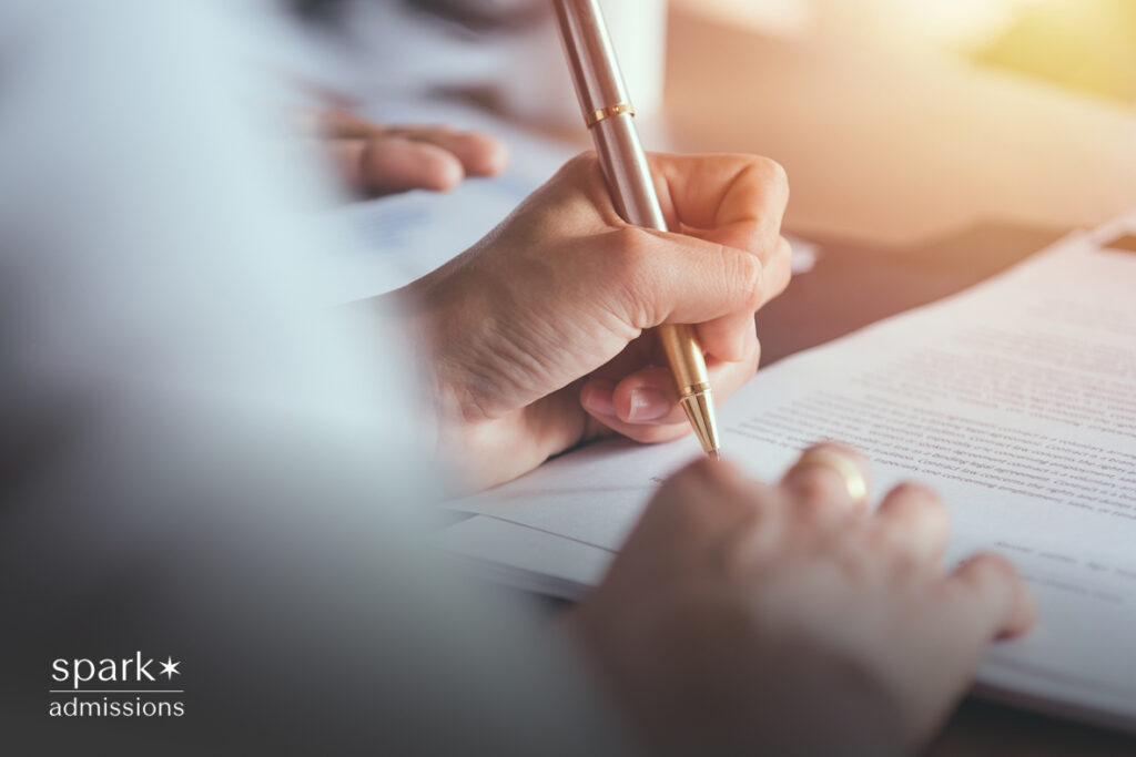 Close-up of a person writing on a document with a pen during an admissions process