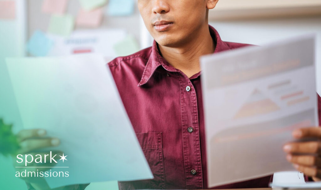 A student in maroon shirt, studies two pages of printed material, focusing on graphs and diagrams